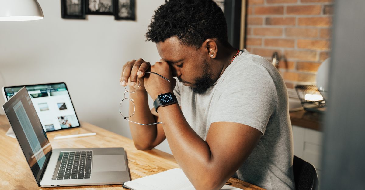 A tired man rubbing his eyes while sitting in front of his laptop