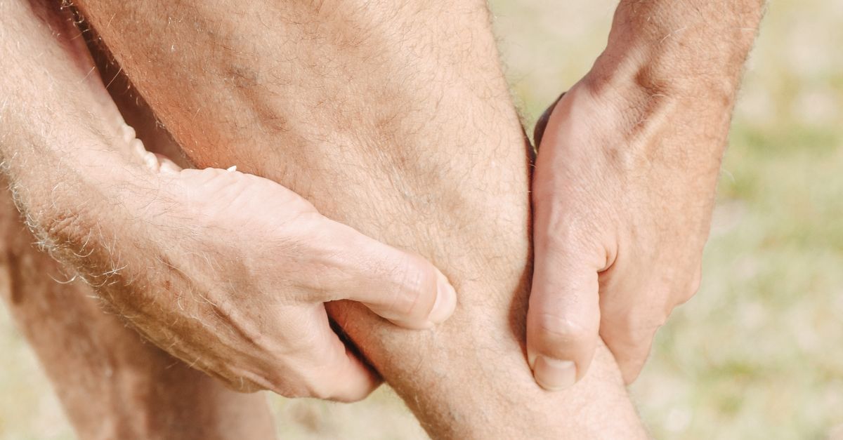 A man massaging his sore calf muscle outdoors