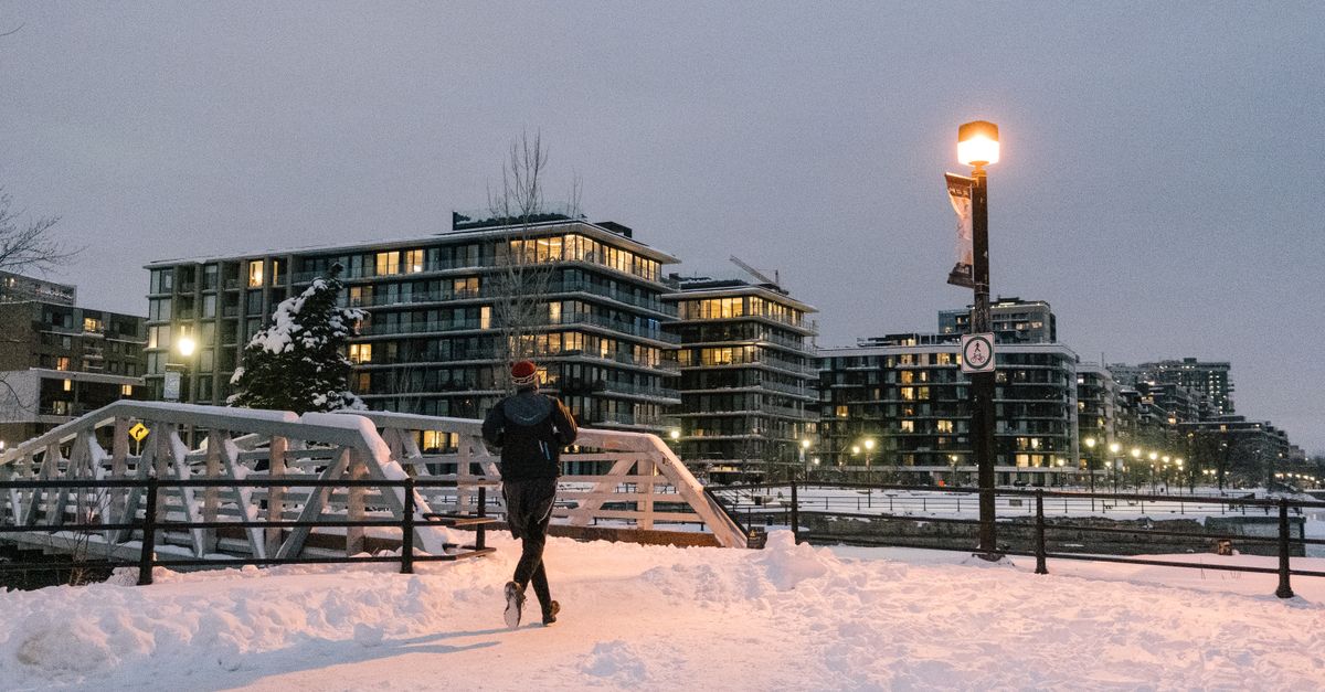 A man running across a snowy city bridge as dusk falls.