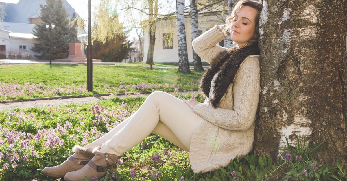 A woman sitting calmly against a tree outdoors
