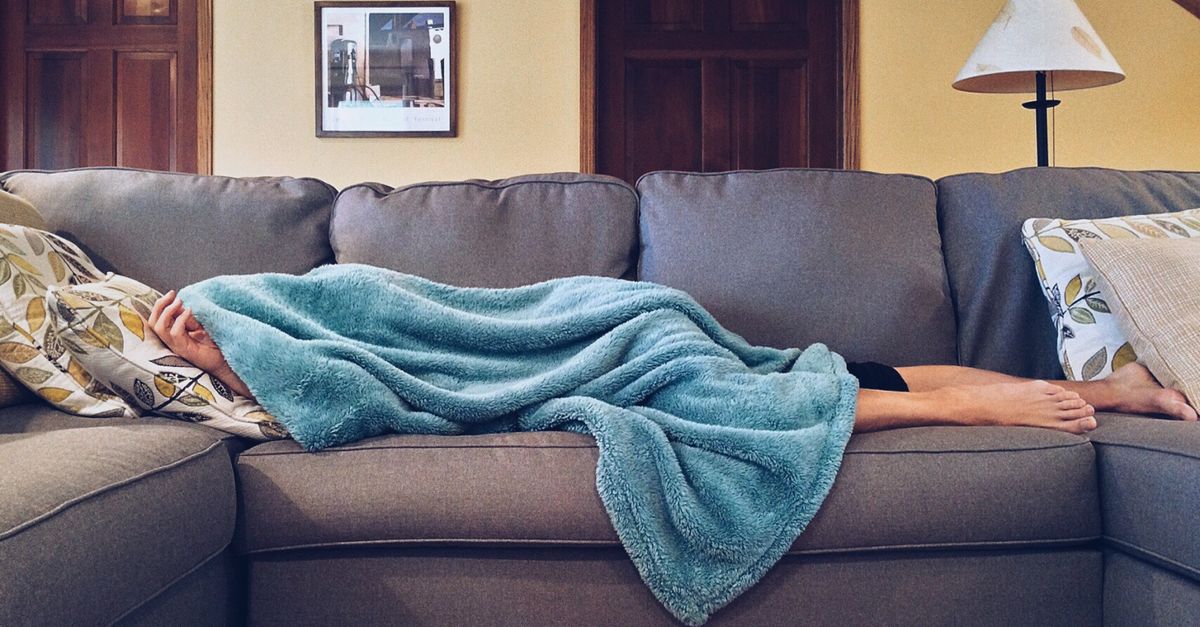 A person resting under a blanket on a sofa