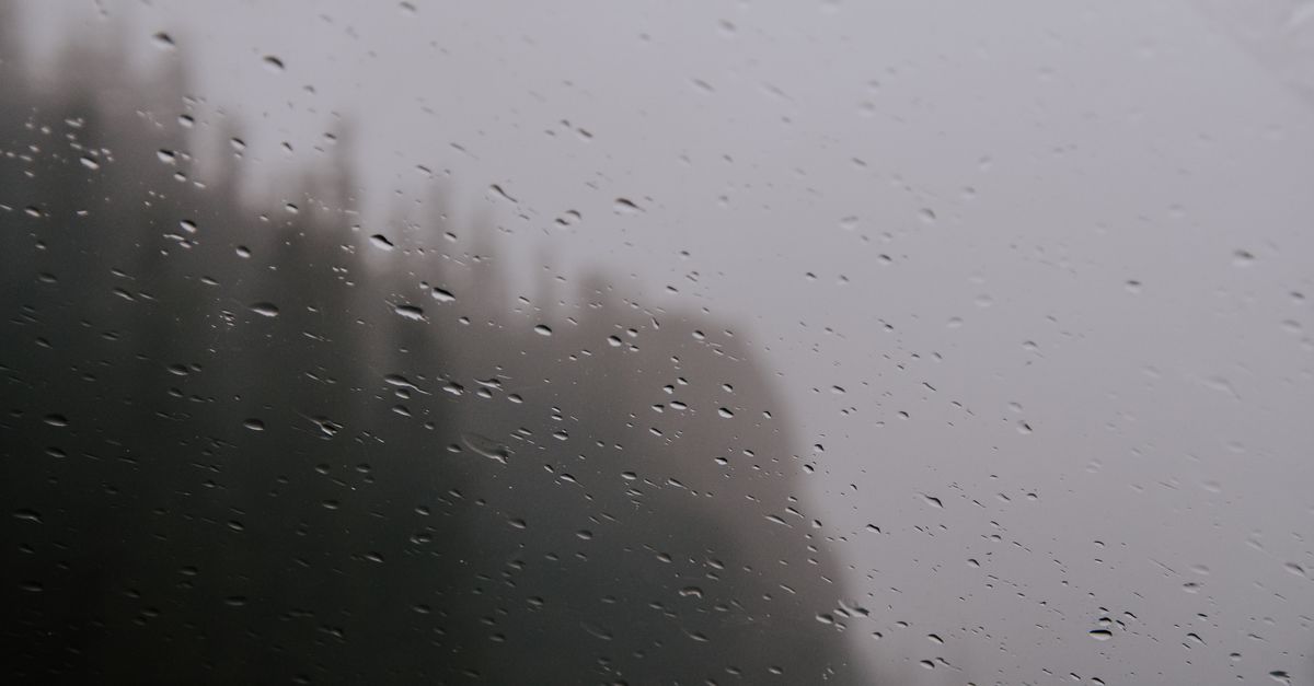 Raindrops on a window with a misty, overcast autumn landscape beyond