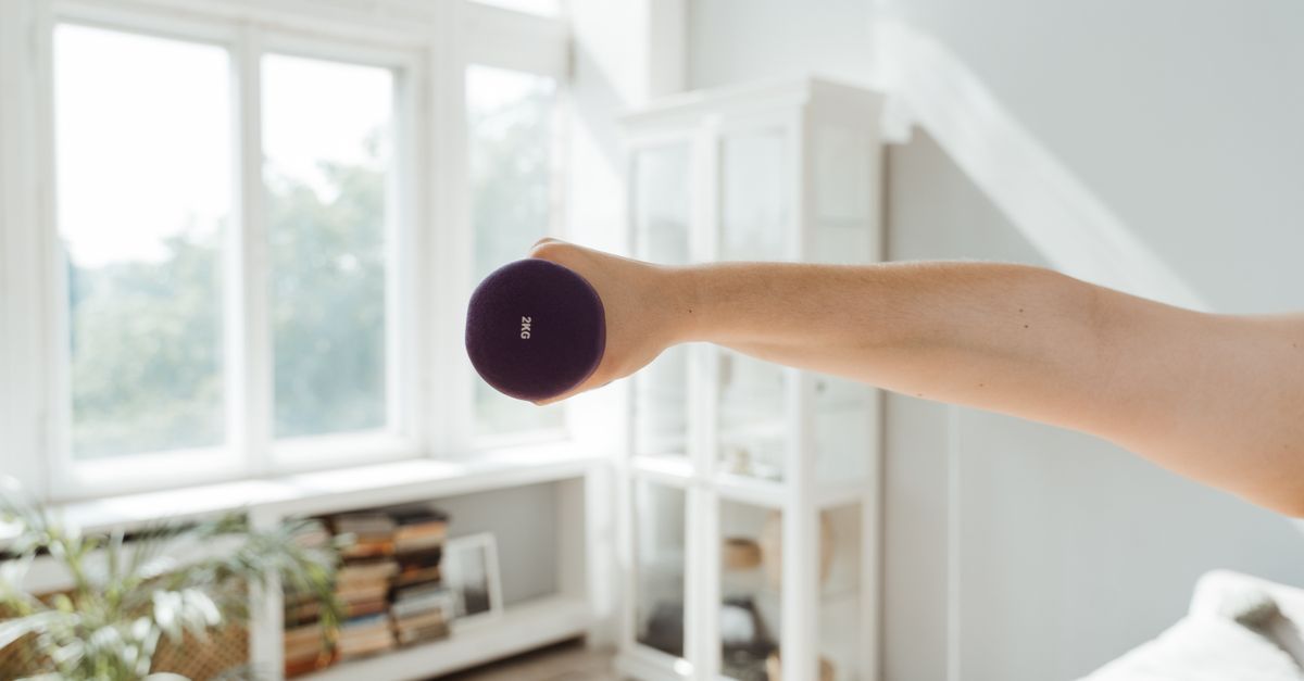 A person lifting a dumbbell in a sunlit room