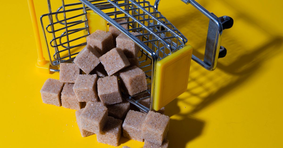 Brown sugar cubes spilling from a small shopping cart on a vibrant yellow background.