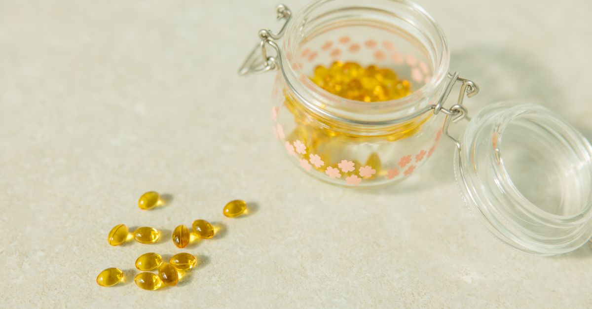 An open glass jar of golden supplement capsules on a pale surface.