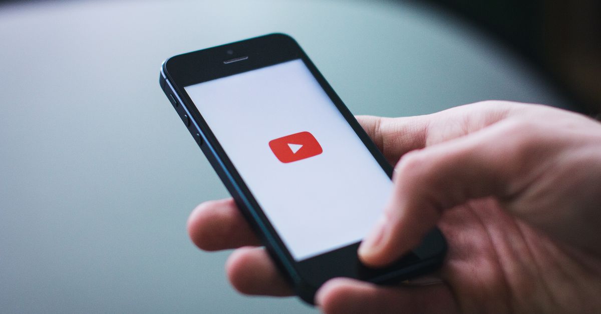 Close-up of a hand holding a smartphone displaying the YouTube app on the screen