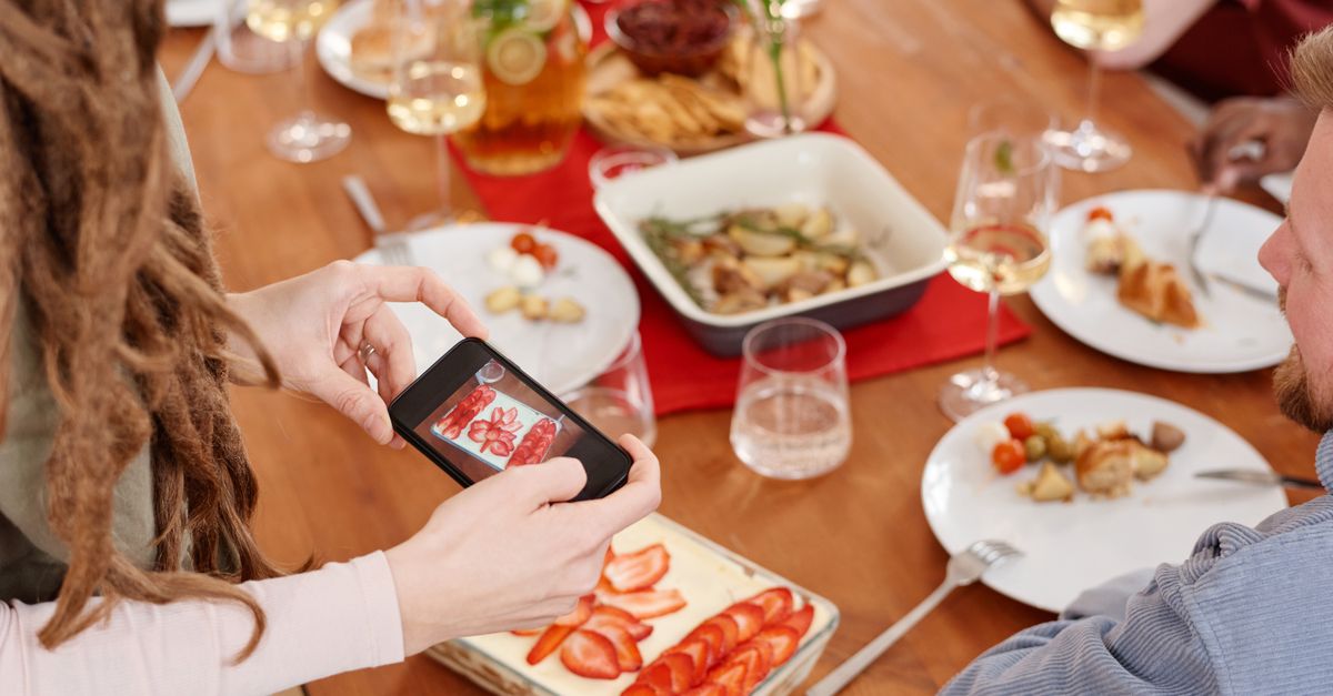 A person photographs a shared meal on their smartphone at the table